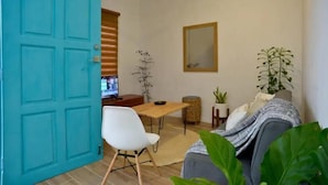 A room with a teal door, a ceiling fan, a dining table with chairs, a sofa, and a potted plant.