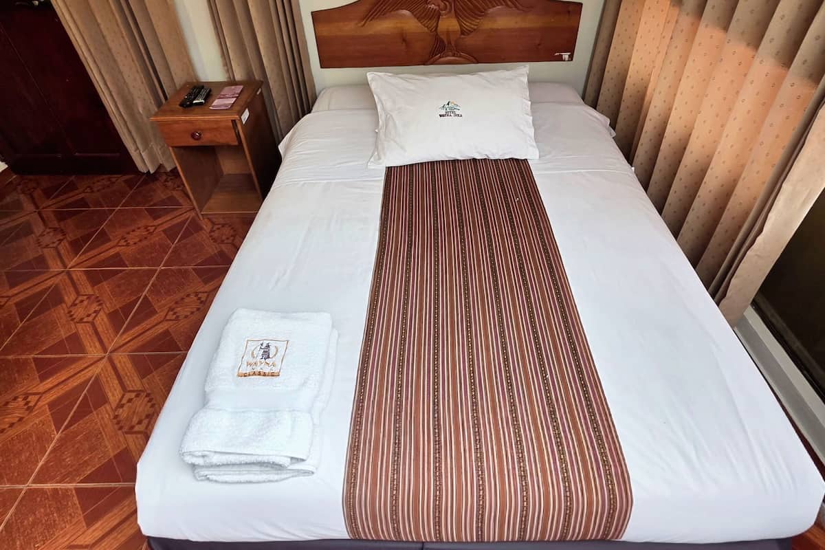 Una cama bien tendida con una manta a rayas, una almohada con un logotipo y una toalla doblada al lado.
