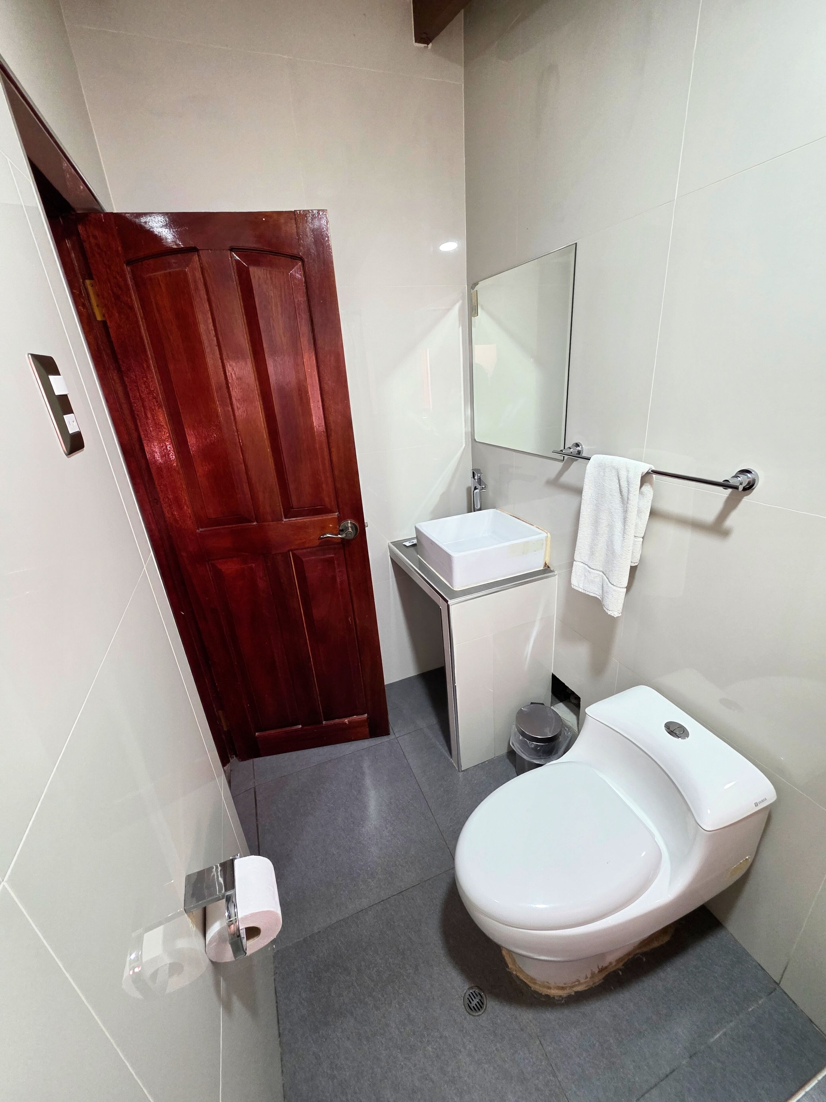 A bathroom with a wooden door, a white sink, a mirror, a towel rack, and a toilet.