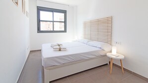 A minimalist bedroom with a bed, bedside table, and a window with blinds.