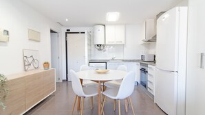 A modern kitchen with white cabinetry, a round dining table with white chairs, and a built-in oven.