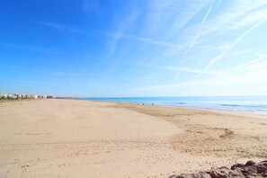 Une vaste plage de sable fin, avec un ciel bleu dégagé et l’océan à l’horizon.
