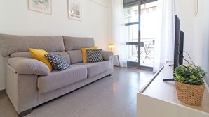A living room with a grey sofa, yellow and patterned cushions, a television, and a plant on a side table.