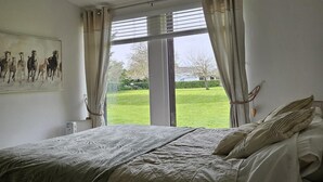 Une chambre avec un grand lit, une fenêtre avec des rideaux et un tableau accroché au mur.