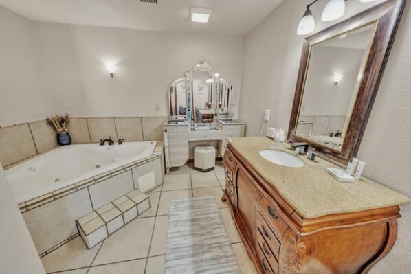 A bathroom with a large bathtub, two sinks, a vanity with a mirror, and a tiled floor.
