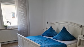 Ein Schlafzimmer mit einem weißen Bett, blauer Bettwäsche und einem Nachttisch mit einer Lampe.