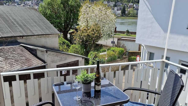 Ein Balkon mit Tisch und zwei Stühlen mit Blick auf einen Fluss und eine Stadt.