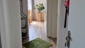 Ein Flur mit Teppich in Grün, einem Metallstuhl, einer Holzschrank und einer Pflanze.