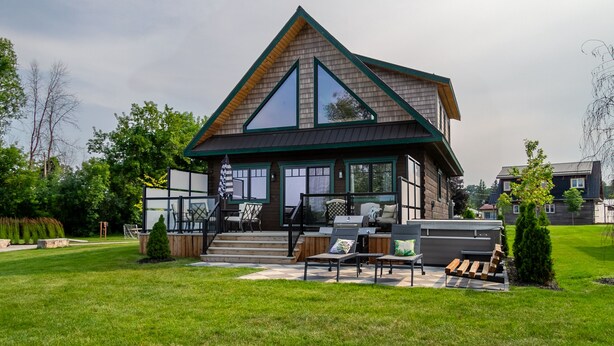 Ein modernes Haus mit einer großen Terrasse, Sitzgelegenheiten im Freien und einem gepflegten Rasen.