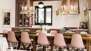 Ein Essbereich mit Holztisch und rosa Stühlen, einer Kandelaber und einer Küche im Hintergrund.