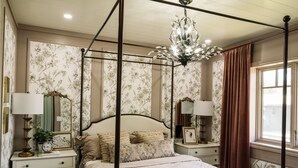 Ein Himmelbett mit einer Chandelüster, Blumenpapier und einem Fenster mit Vorhängen.