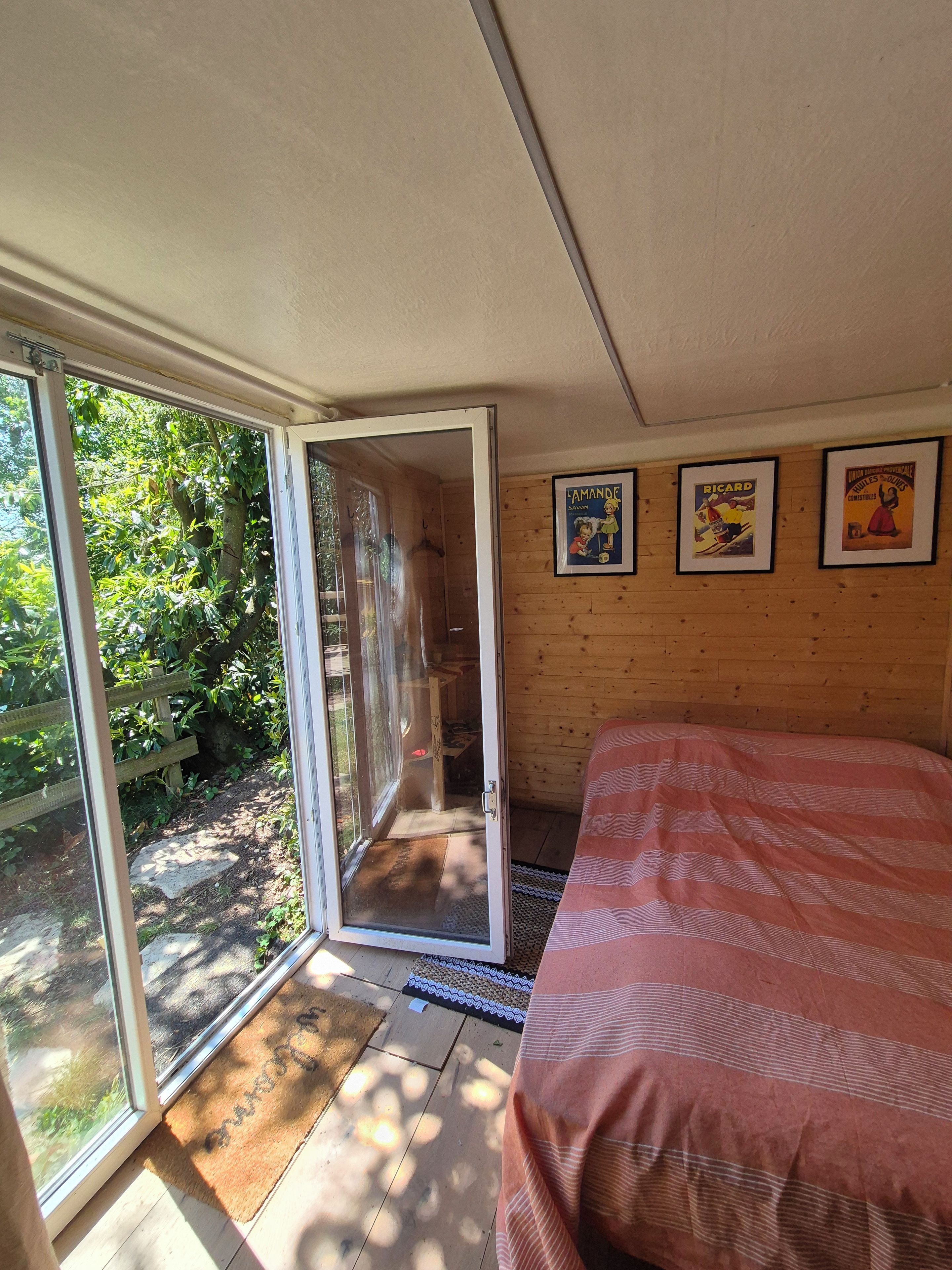 Quarto com cama, porta de vidro deslizante para um jardim e três cartazes emoldurados na parede.