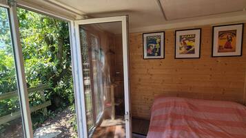 Quarto com cama, porta de vidro deslizante para um jardim e três cartazes emoldurados na parede.