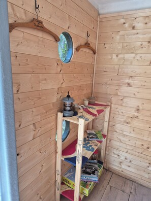 A wooden interior with a shelf holding books and a small table with a kettle.