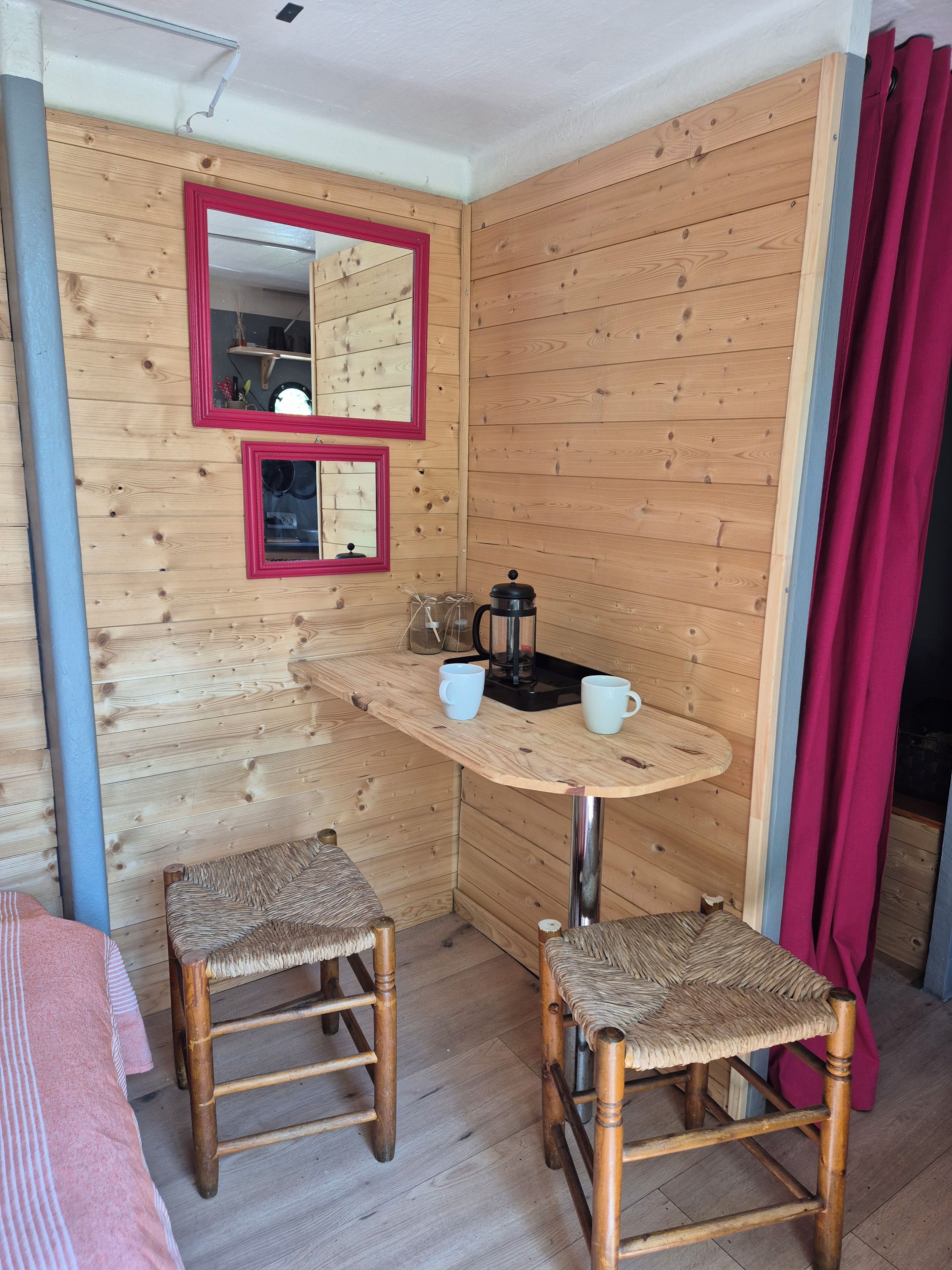 Ein kleiner Holzraum mit einem Tisch, zwei Stühlen, einer Kaffeemaschine und einem Spiegel.
