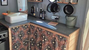 Una cocina compacta con un lavamanos, estufa y varios utensilios. Hay repisas sobre la encimera con frascos y una tetera.