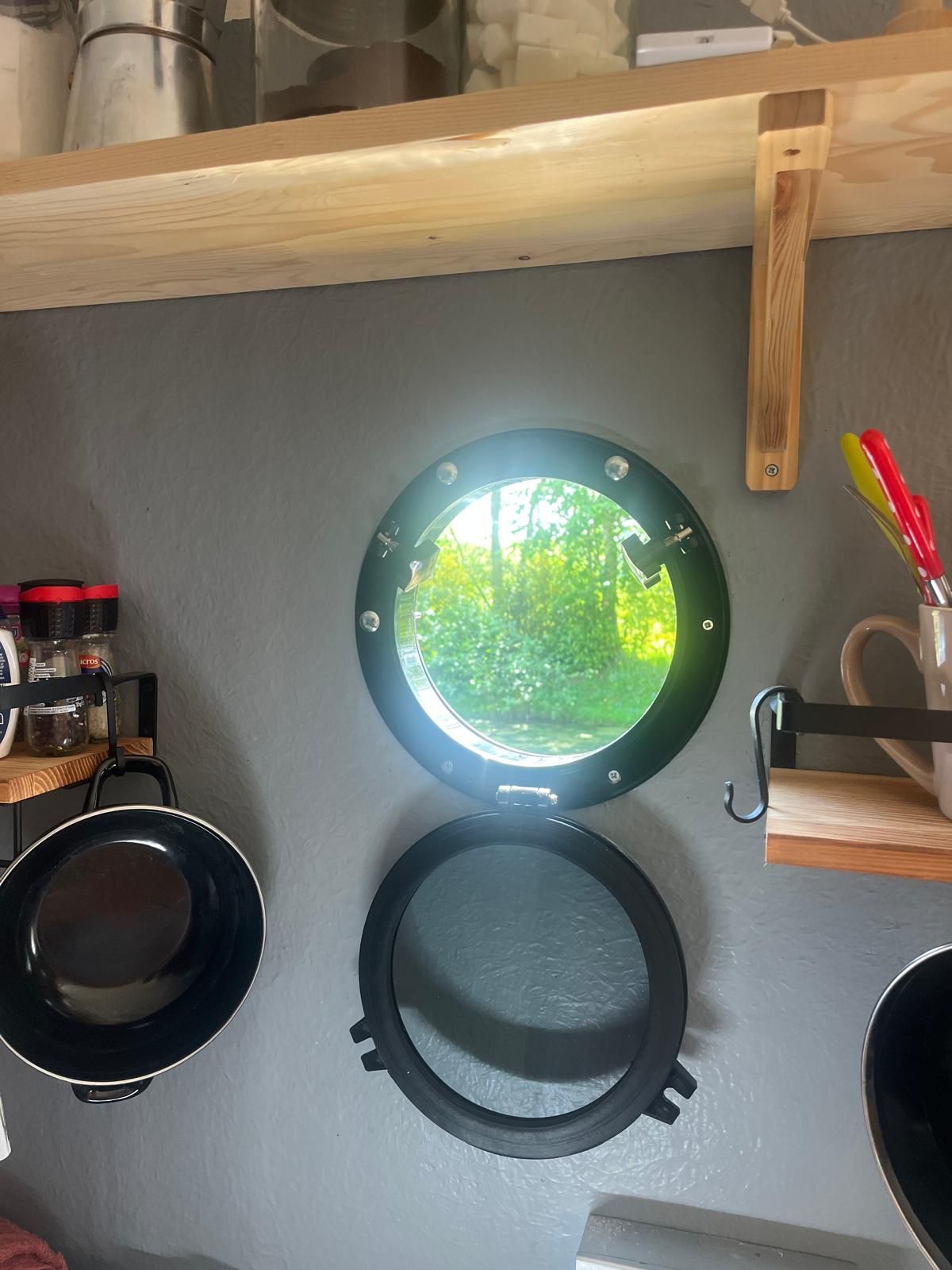 Eine Küche mit rundem Fenster, einer schwarzen Bratpfanne und einem Holzboden.