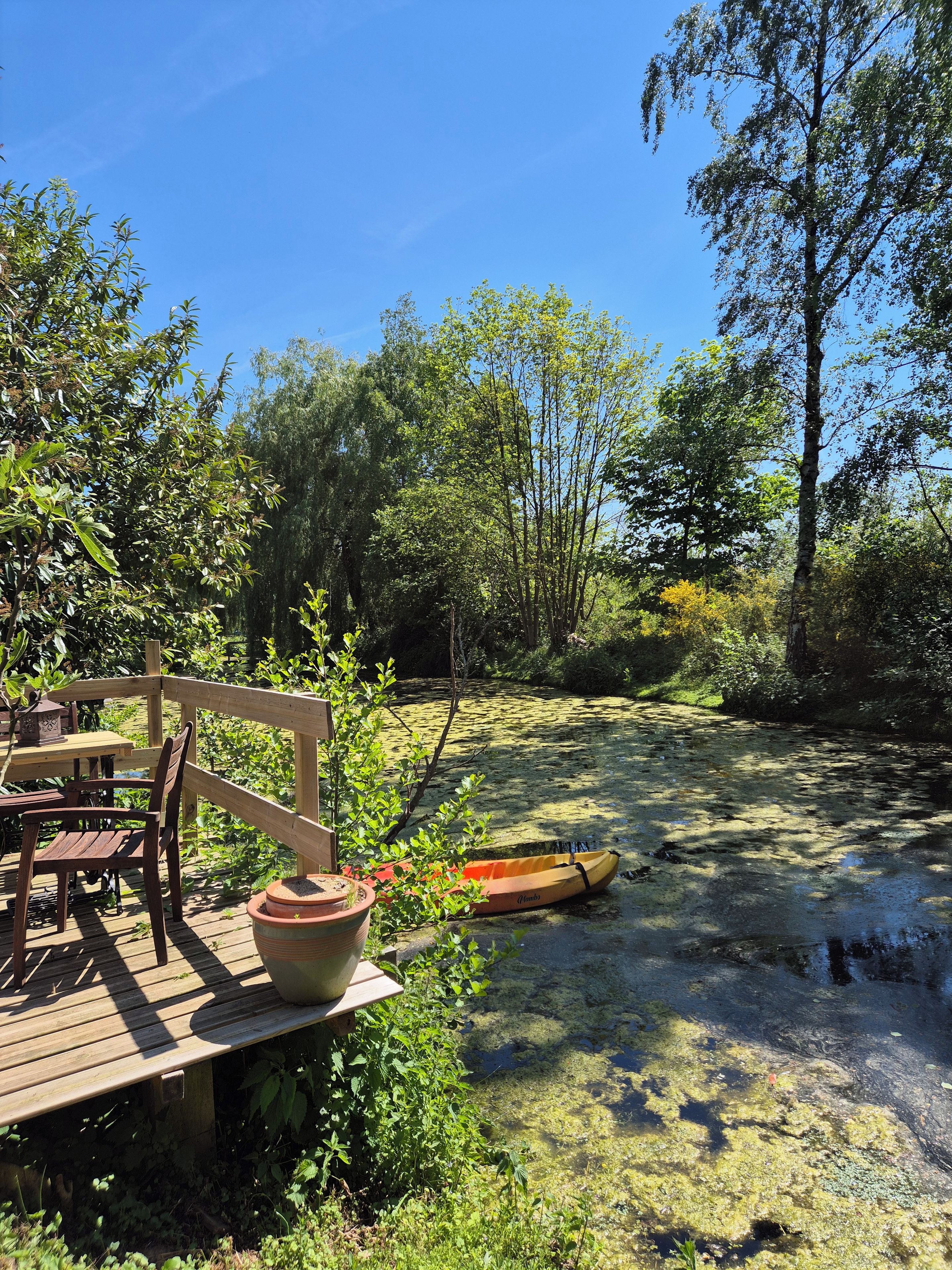 Una terraza de madera con una mesa, sillas, un kayak y un estanque.
