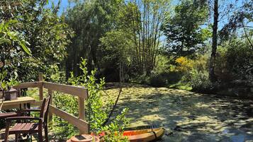 Una terraza de madera con una mesa, sillas, un kayak y un estanque.