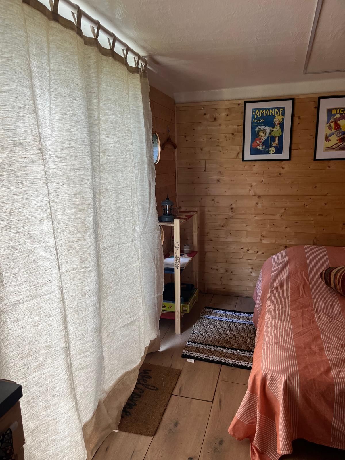 Une pièce avec un lit, une étagère en bois, un rideau et une affiche accrochée au mur.