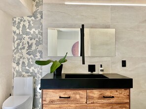 Een moderne badkamer met toilet, wastafel met zwart aanrecht, houten kast en spiegel met decoratief element.