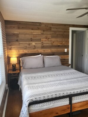A bedroom with a wooden headboard, a bed with patterned bedding, a bedside table with a lamp, and a door to the right.
