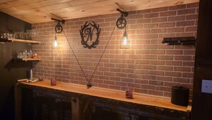 A bar area with a brick wall, hanging light fixtures, and shelves with glasses and bottles. - POND IN THE PINES CABIN -COMPLETELY RENOVATED ON 27 ACRES - POND-HOCKING HILLS (McArthur)