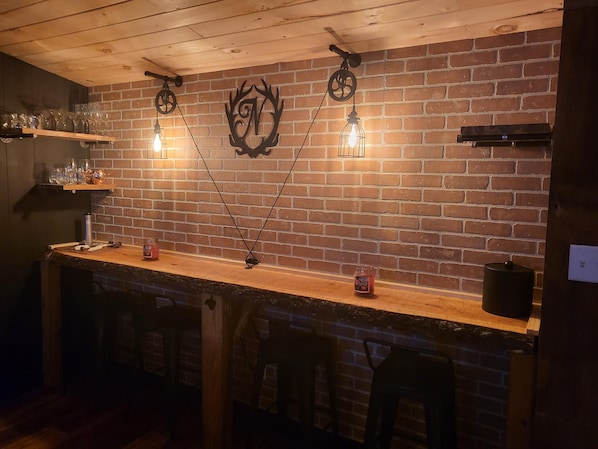 A bar area with a brick wall, hanging light fixtures, and shelves with glasses and bottles.