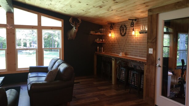A cozy room with a wooden ceiling, a leather sofa, a brick fireplace, and a deer head mounted on the wall. - POND IN THE PINES CABIN -COMPLETELY RENOVATED ON 27 ACRES - POND-HOCKING HILLS (McArthur)