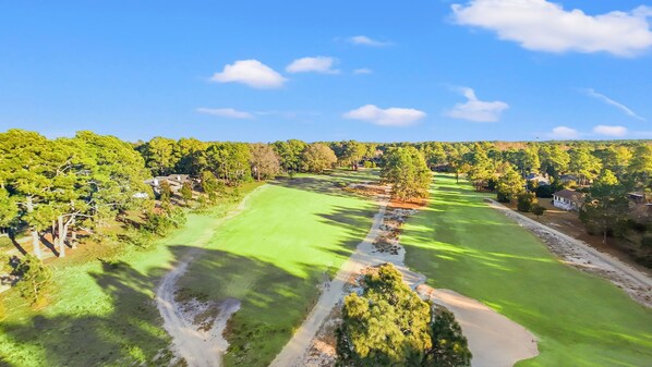 A golf course with a clear path, surrounded by trees and houses.