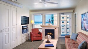 A living room with a fireplace, a television, a red armchair, a sofa, and a view of the ocean through large windows. - Worldmark Seaside, Beachfront Resort!! Add Nights 5, 6 &7 only 50 each. (Seaside)