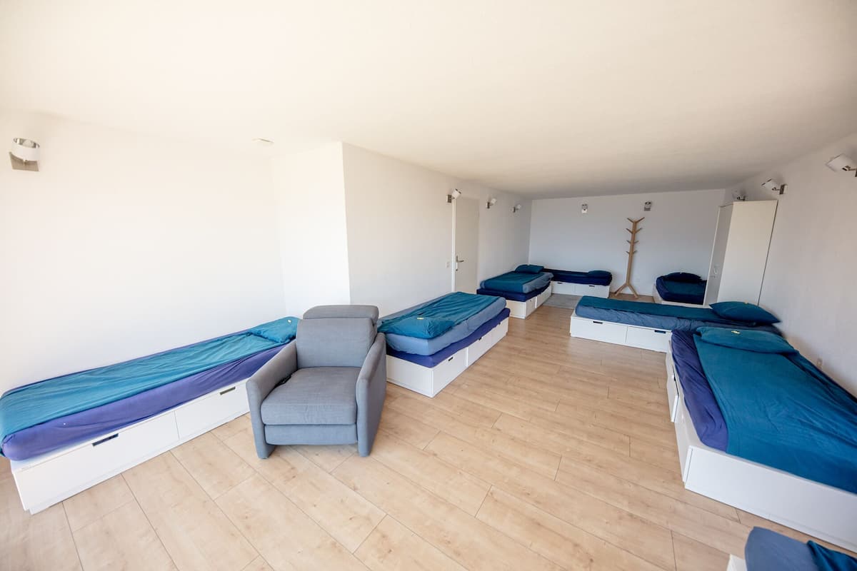 Une chambre de dortoir avec quatre lits simples, une chaise grise et un porte-manteau.