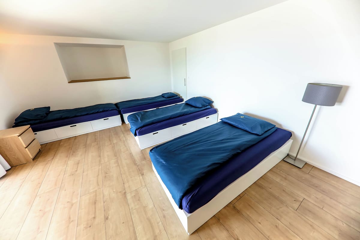Une chambre avec trois lits, un plancher en bois, un bureau et une lampe.