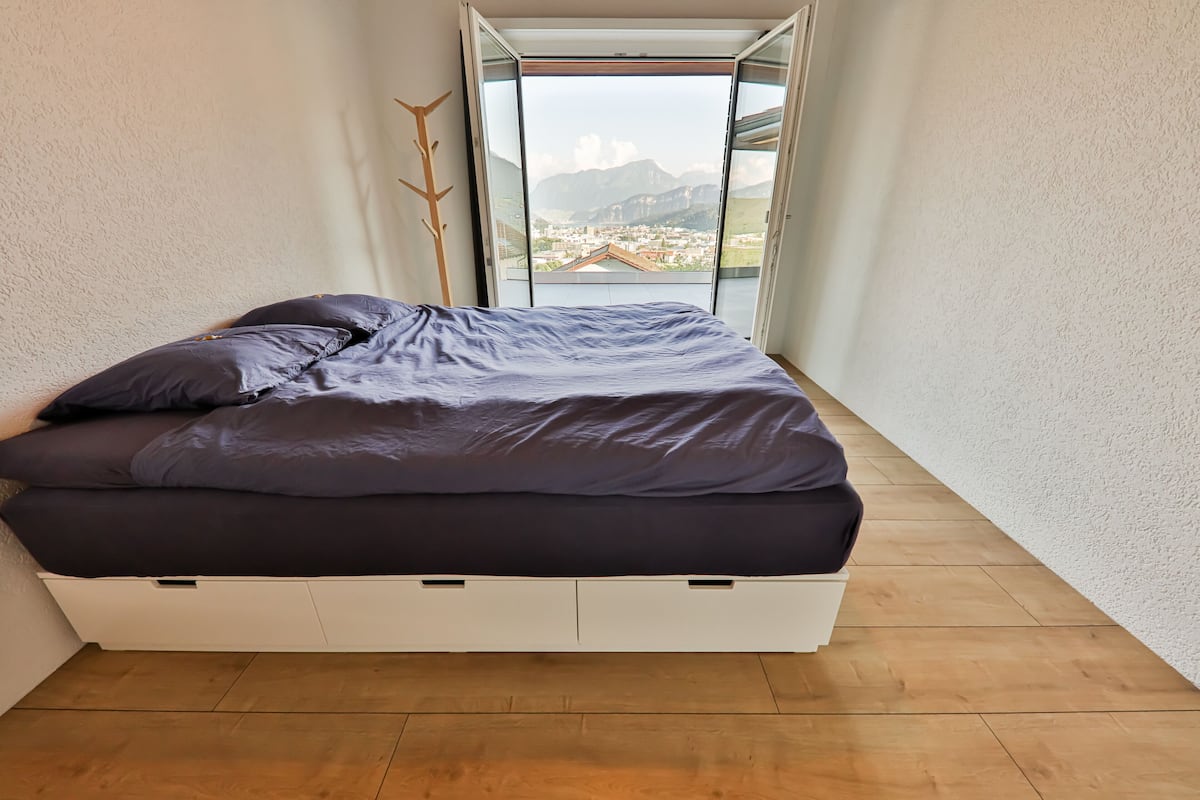 Une chambre à coucher avec un lit, une vue sur les montagnes et un mur blanc.