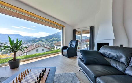 A modern living room with a chessboard, a leather sofa, a chair, and a view of mountains through large windows.