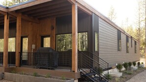 Una casa moderna de un piso con porche cubierto, una parrilla y una escalera que lleva a una terraza.