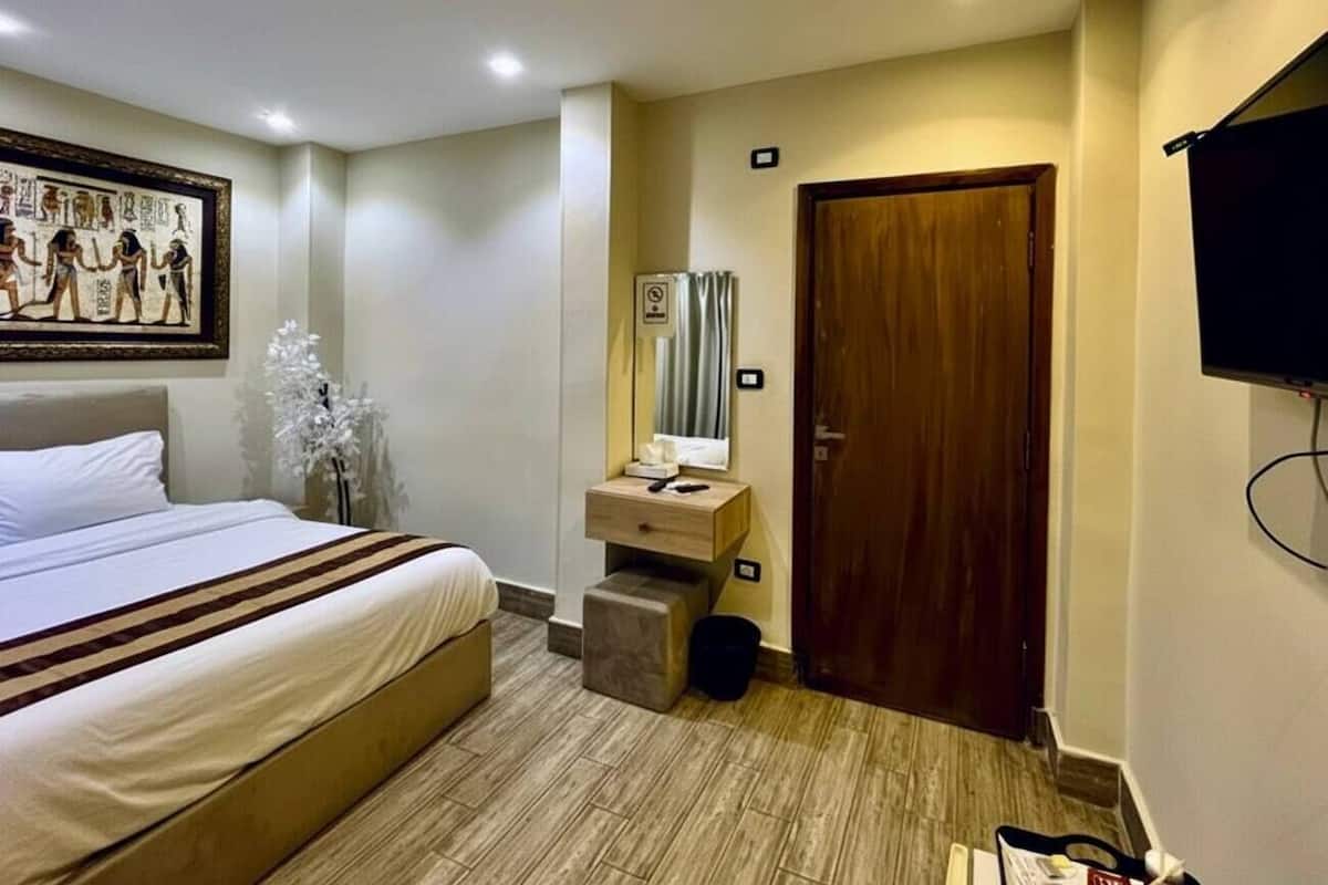 A hotel room with a bed, a small bedside table, a mirror, and a television mounted on the wall.