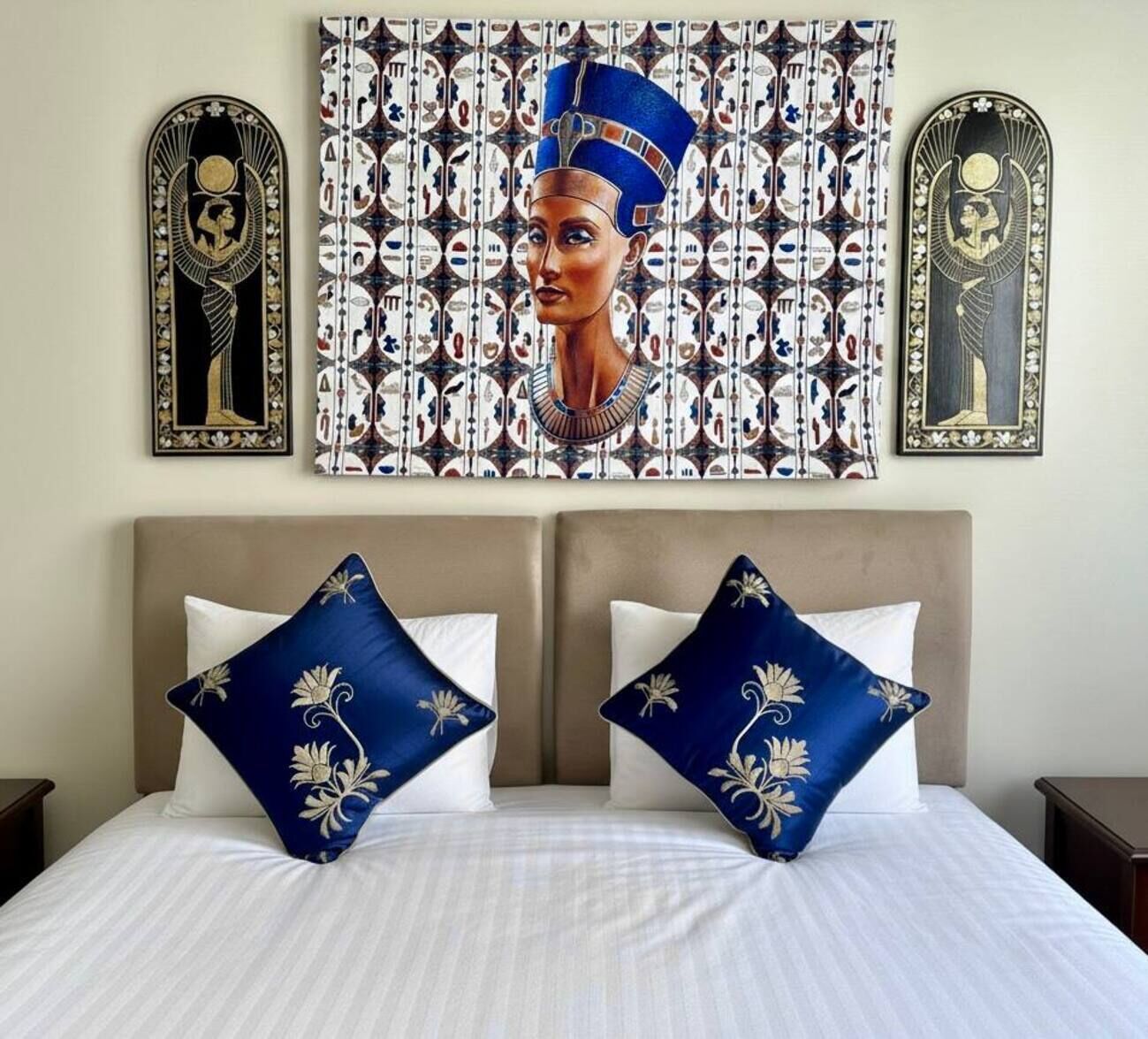 A hotel room with a bed, two pillows, a headboard, and a wall tapestry.