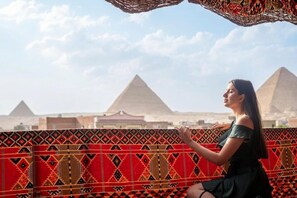A person sitting on a balcony with a patterned wall and a view of pyramids. - King of Pharaohs Pyramids View (Giza)