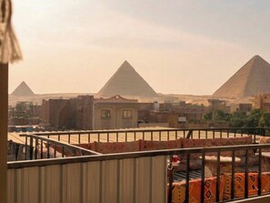 A view of the pyramids from a balcony with a metal railing and patterned cushions. - King of Pharaohs Pyramids View (Giza)