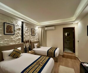 A hotel room with two beds, a marble wall, a mirror, and a bathroom visible through an open door. - King of Pharaohs Pyramids View (Giza)