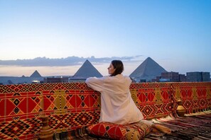A person sitting on a patterned couch with a view of pyramids in the background. - King of Pharaohs Pyramids View (Giza)