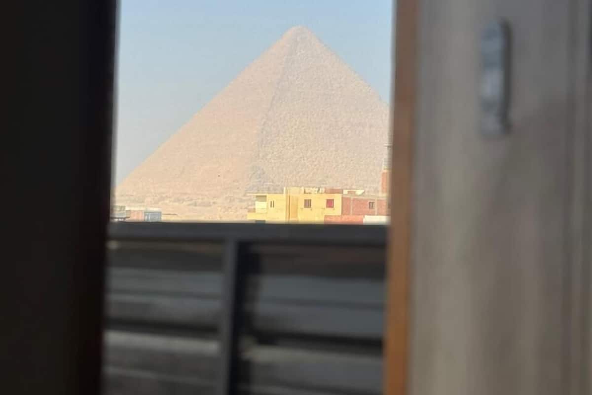 A view of the Great Pyramid of Giza from inside a building, with a clear sky and a few buildings in the foreground.