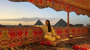 A person sitting on a patterned floor with a view of pyramids in the background. - King of Pharaohs Pyramids View (Giza)