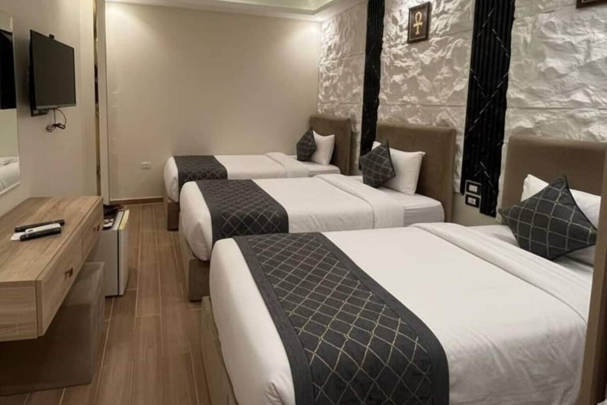 A hotel room with three beds, a desk, and a television.