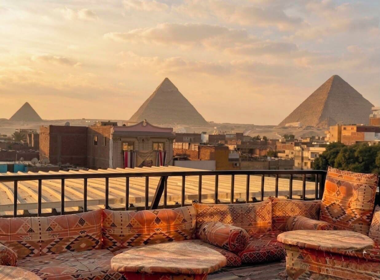 Una terraza en la azotea con vistas a dos pirámides, barandilla y cojines estampados.