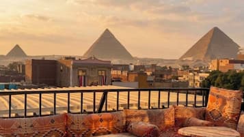 A rooftop terrace with a view of two pyramids, a railing, and patterned cushions.