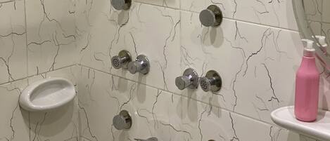 A bathroom with a shower, multiple faucets, a sink, and a mirror.