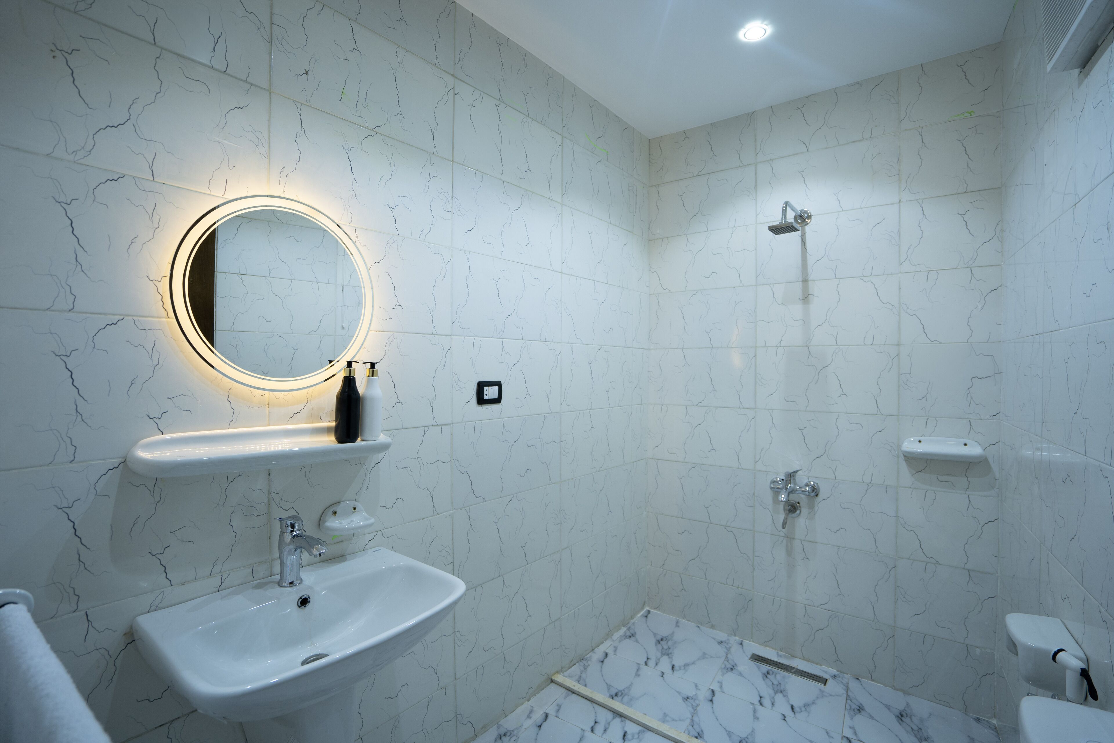 A modern bathroom with a marble sink, a round mirror with a light, a shower, and a toilet.