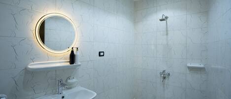 A modern bathroom with a marble sink, a round mirror with a light, a shower, and a toilet.